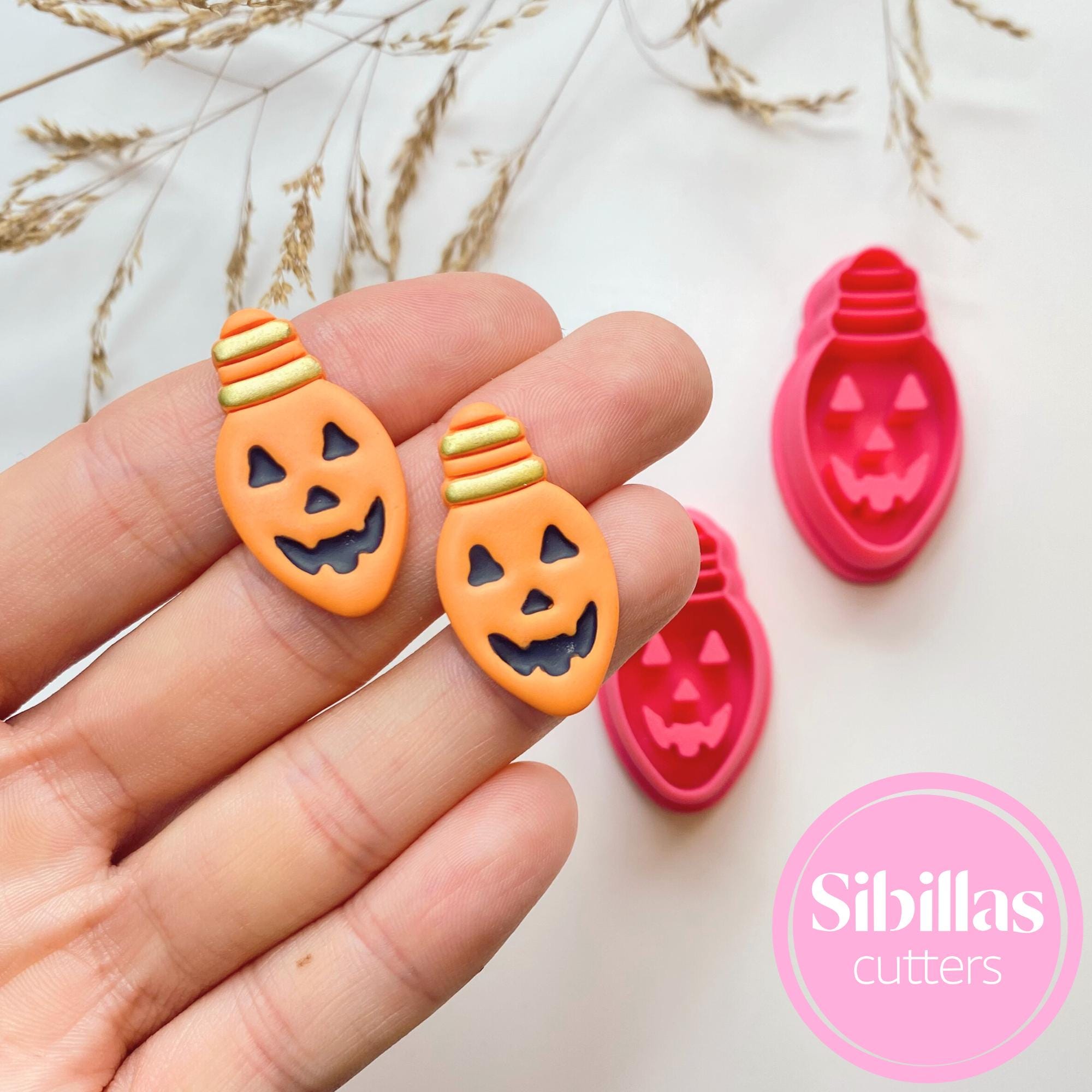 Halloween-themed cookie cutters shaped like jack-o'-lanterns and light bulbs held by a hand with 'Sibillas cutters' branding.