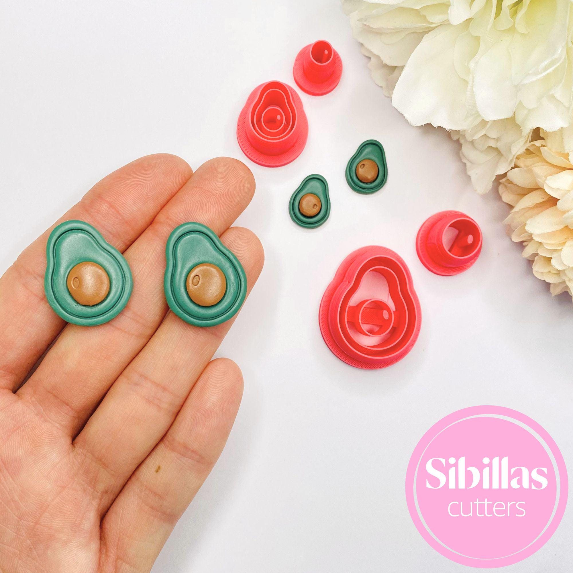 Avocado-shaped cookie cutters on a white surface with flowers, held by a hand.