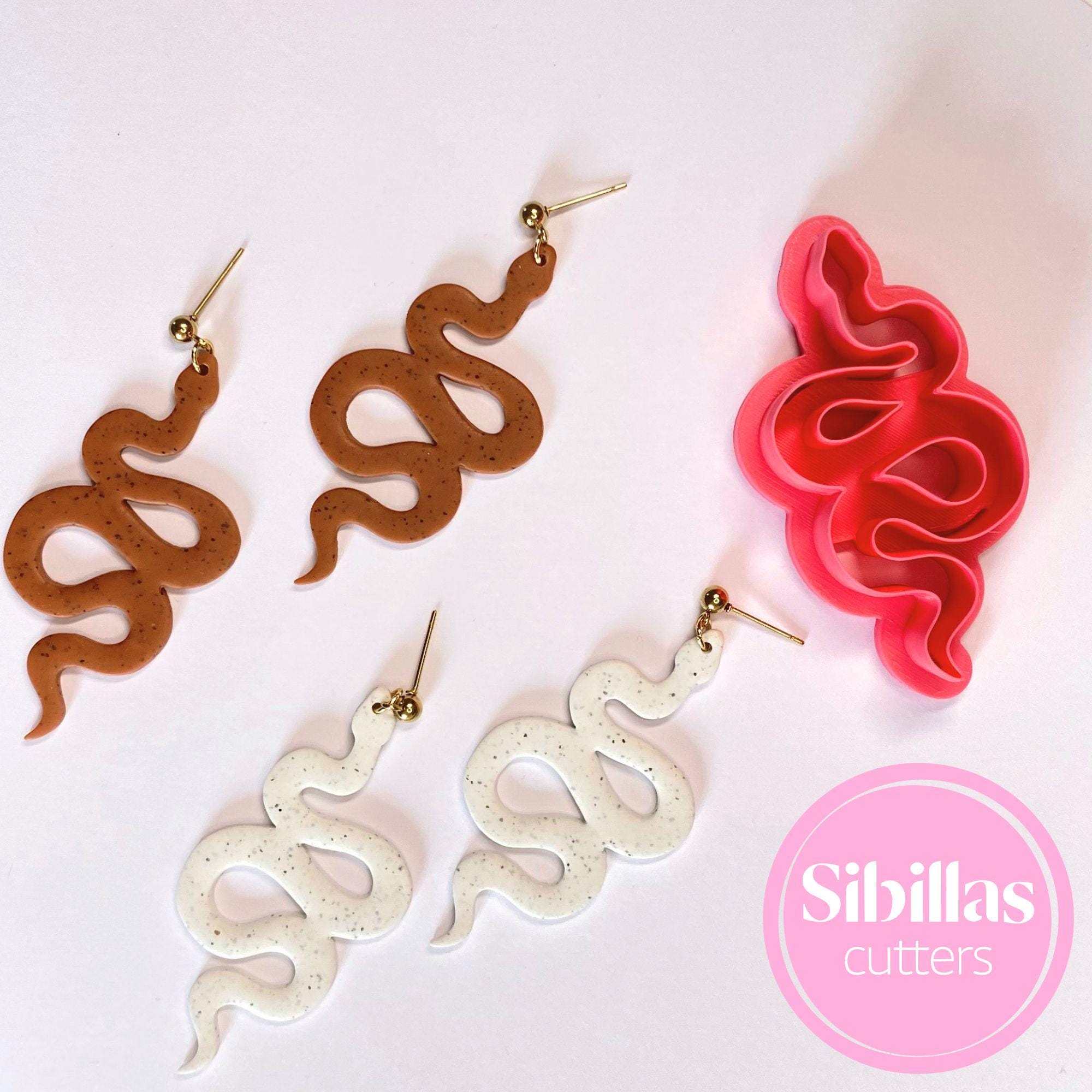 Snake-shaped cookie cutters in brown, red, and white on a light pink background with 'Sibillas cutters' branding.