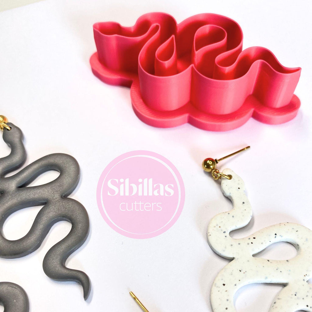 Red silicone mold shaped like a snake, with gray and white snake-shaped objects and 'Sibillas cutters' branding.