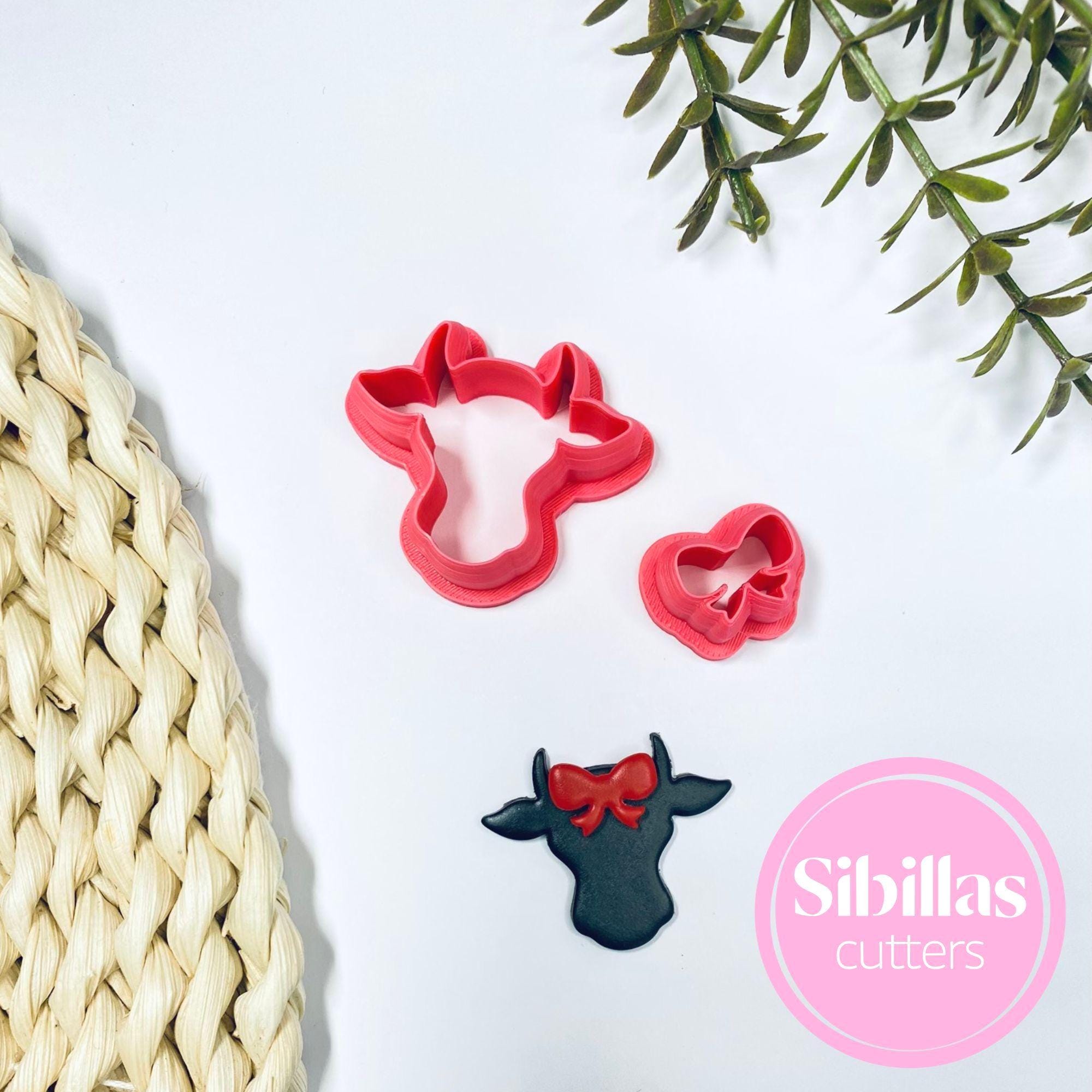 Red cow-shaped cookie cutter with a black cow decoration on a white surface, featuring the brand 'Sibillas cutters'.