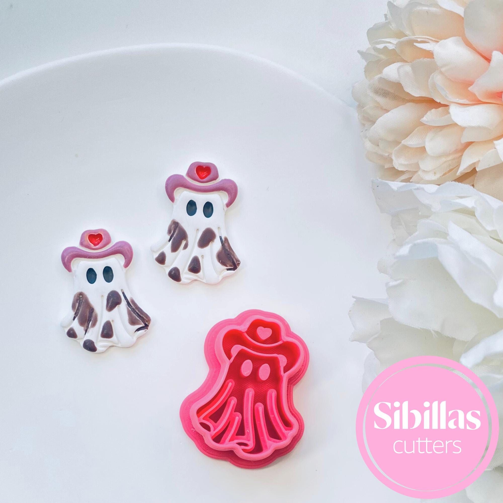 Cowgirl-themed cookie cutters on a white plate with flowers in the background, featuring the brand 'Sibillas'.