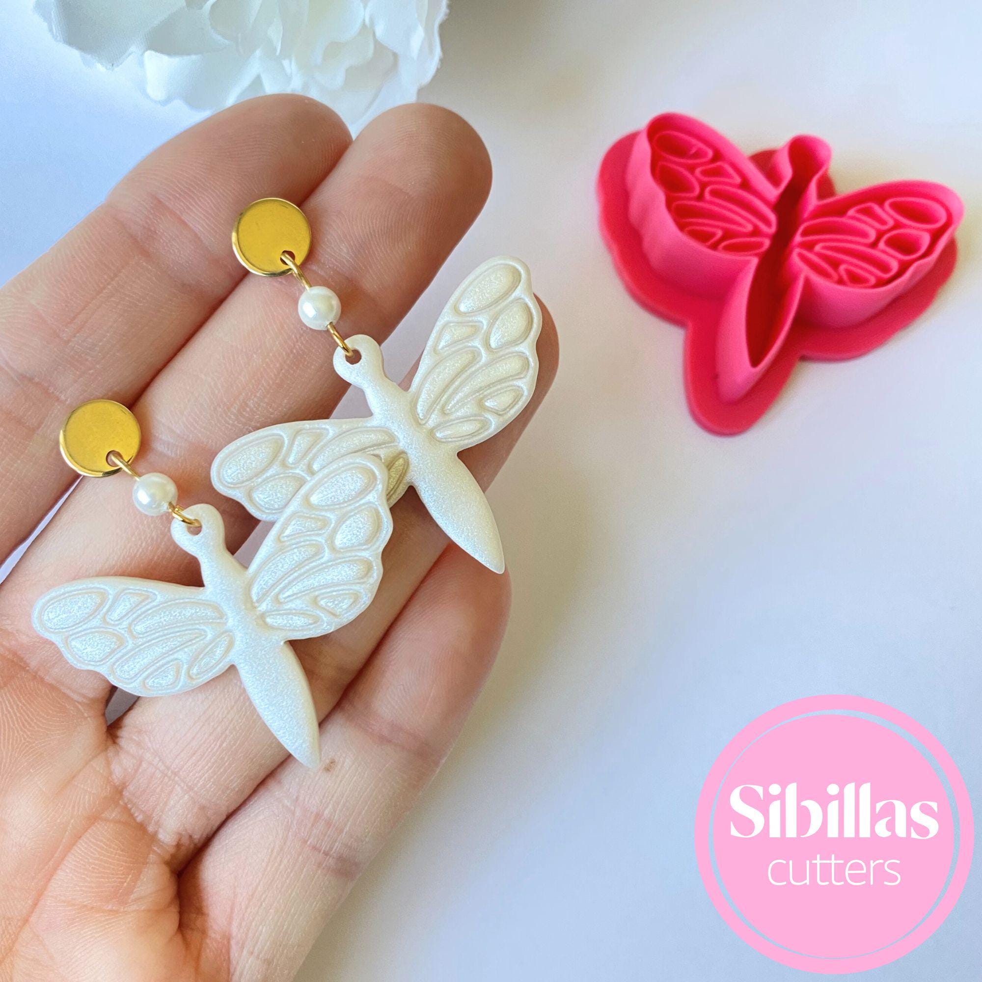 Butterfly-shaped cookie cutters held by a hand with a pink 'Sibillas cutters' logo.