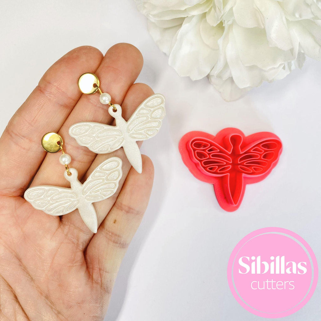Butterfly-shaped cookie cutters held in a hand with a white flower in the background, branded 'Sibillas Cutters'.