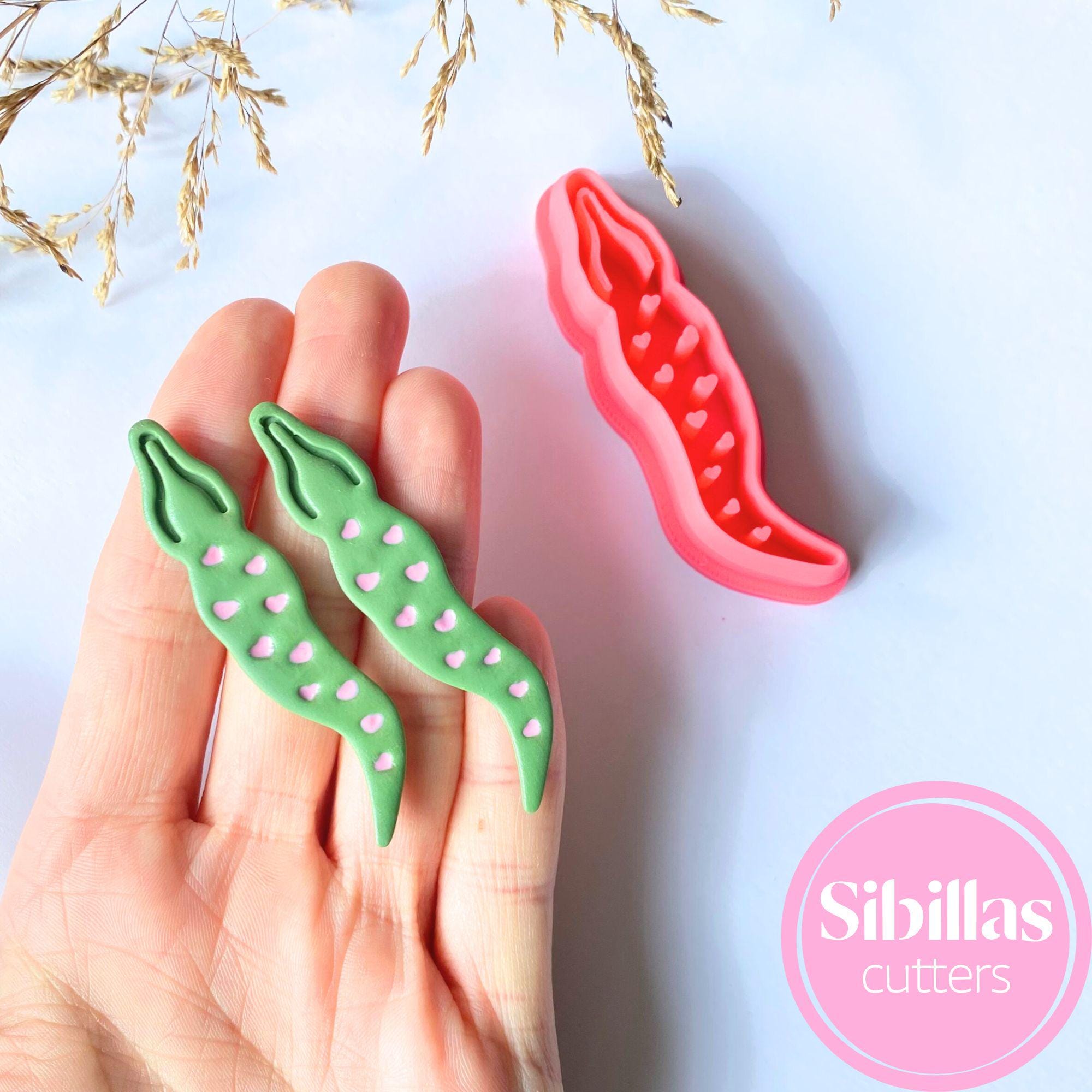 Two green and one red vegetable-shaped cookie cutters held in a hand with a light blue background and 'Sibillas cutters' branding.