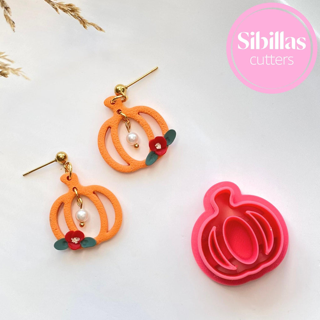 Pumpkin-shaped earrings with decorative elements and a matching pink pumpkin cutter on a white background.