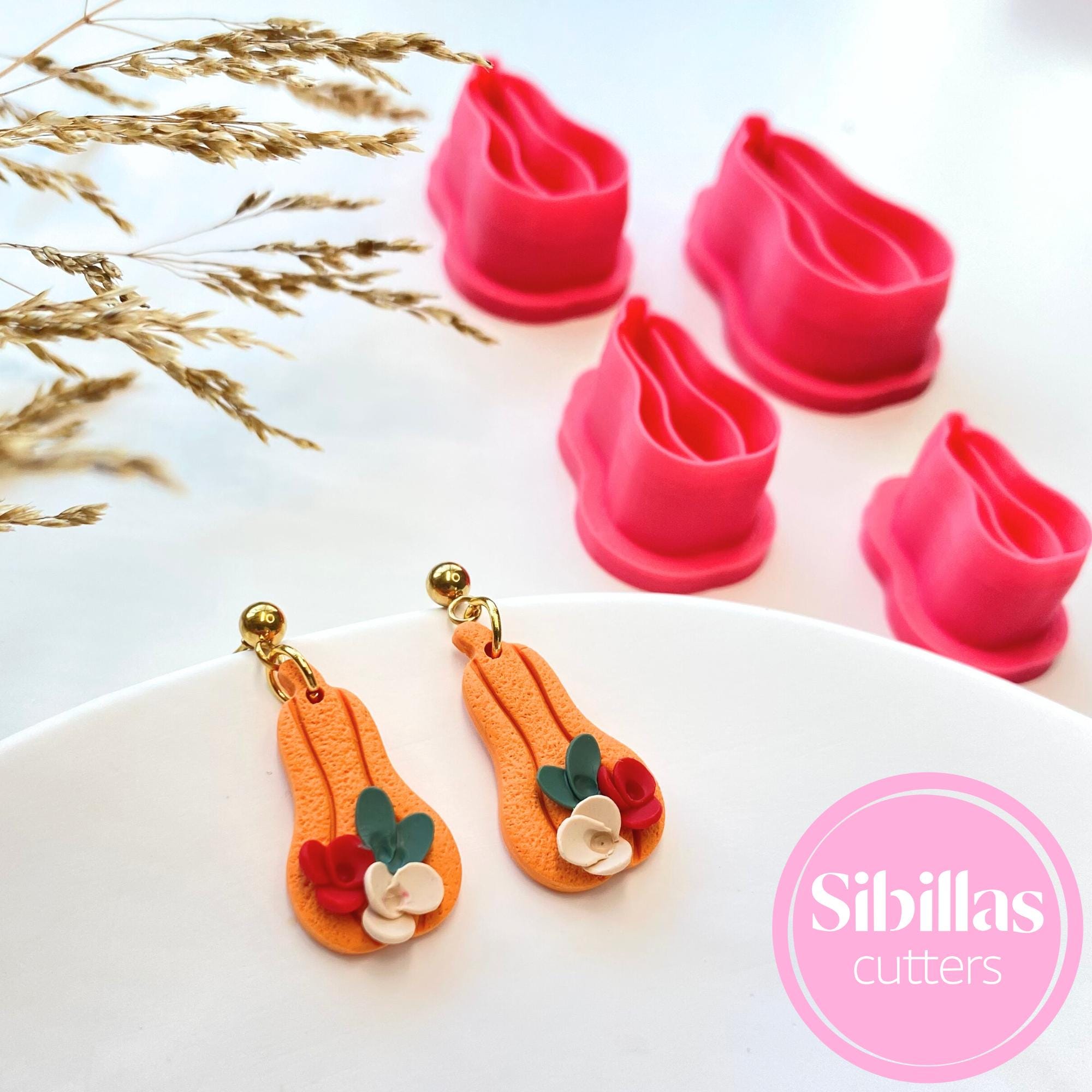 Colorful cookie cutters shaped like flowers on a white plate with 'Sibillas Cutters' branding.