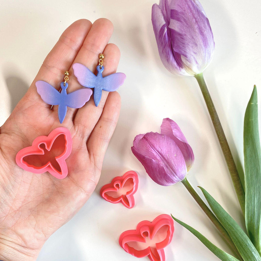 Butterfly-shaped cookie cutters with a hand holding them and a purple tulip on a light background
