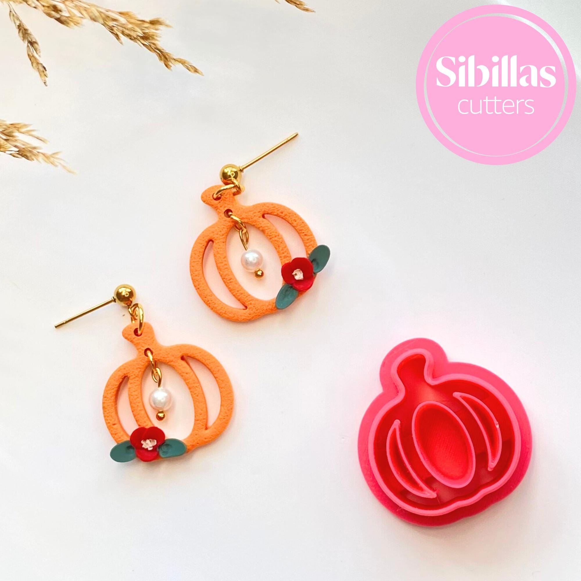 Pumpkin-shaped earrings with floral details and a matching pink pumpkin cutter on a white background.