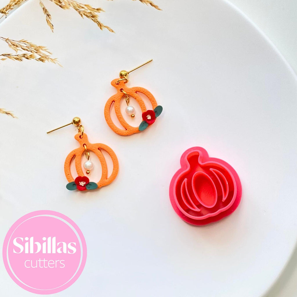Pumpkin-shaped earrings with a matching pink cutter on a white plate, featuring the brand 'Sibillas Cutters'.
