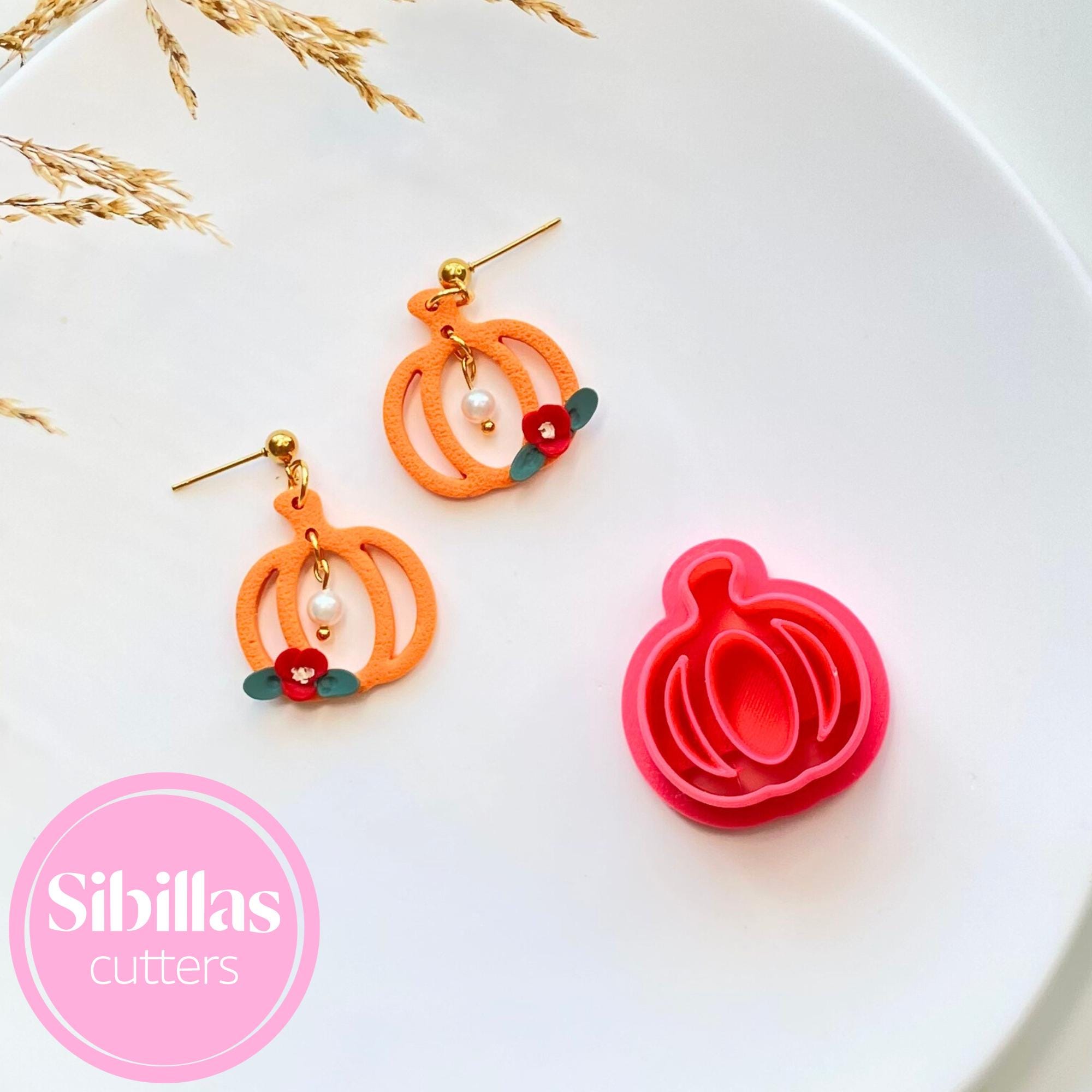 Pumpkin-shaped earrings with a matching pink cutter on a white plate, featuring the brand 'Sibillas Cutters'.