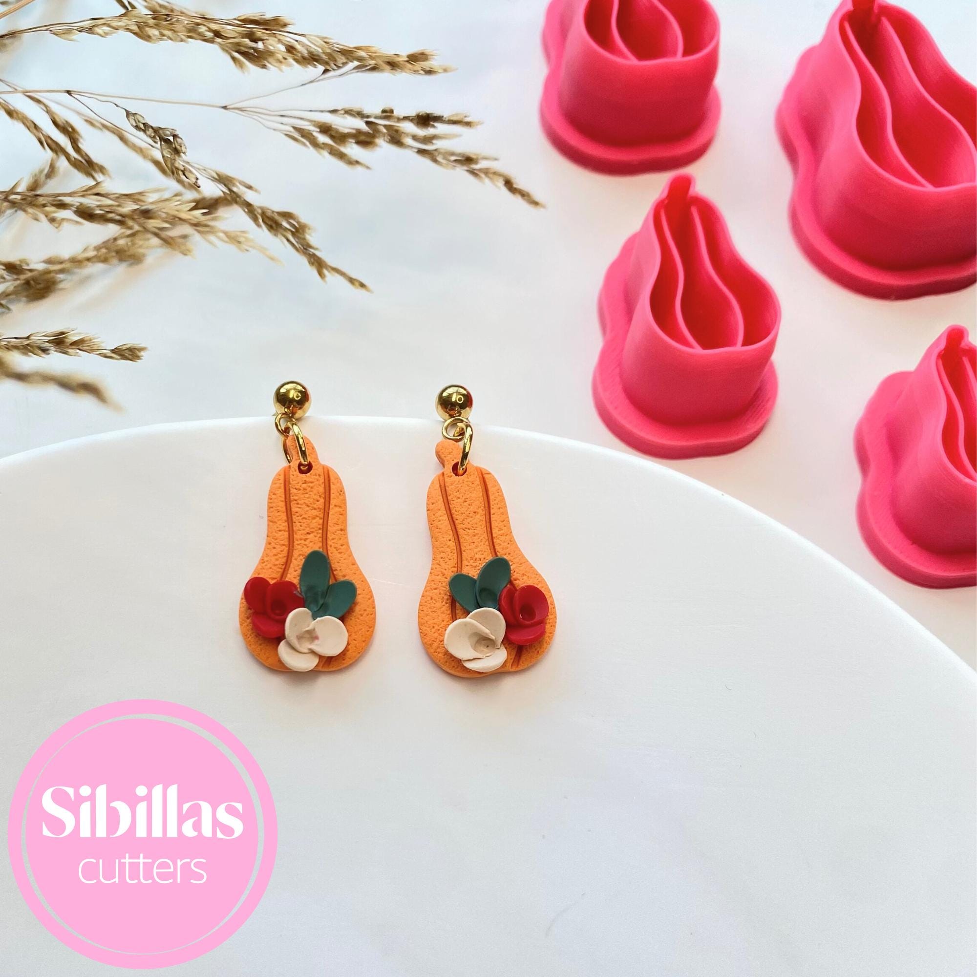 Decorative earrings with floral details on a white plate, surrounded by pink cookie cutters.