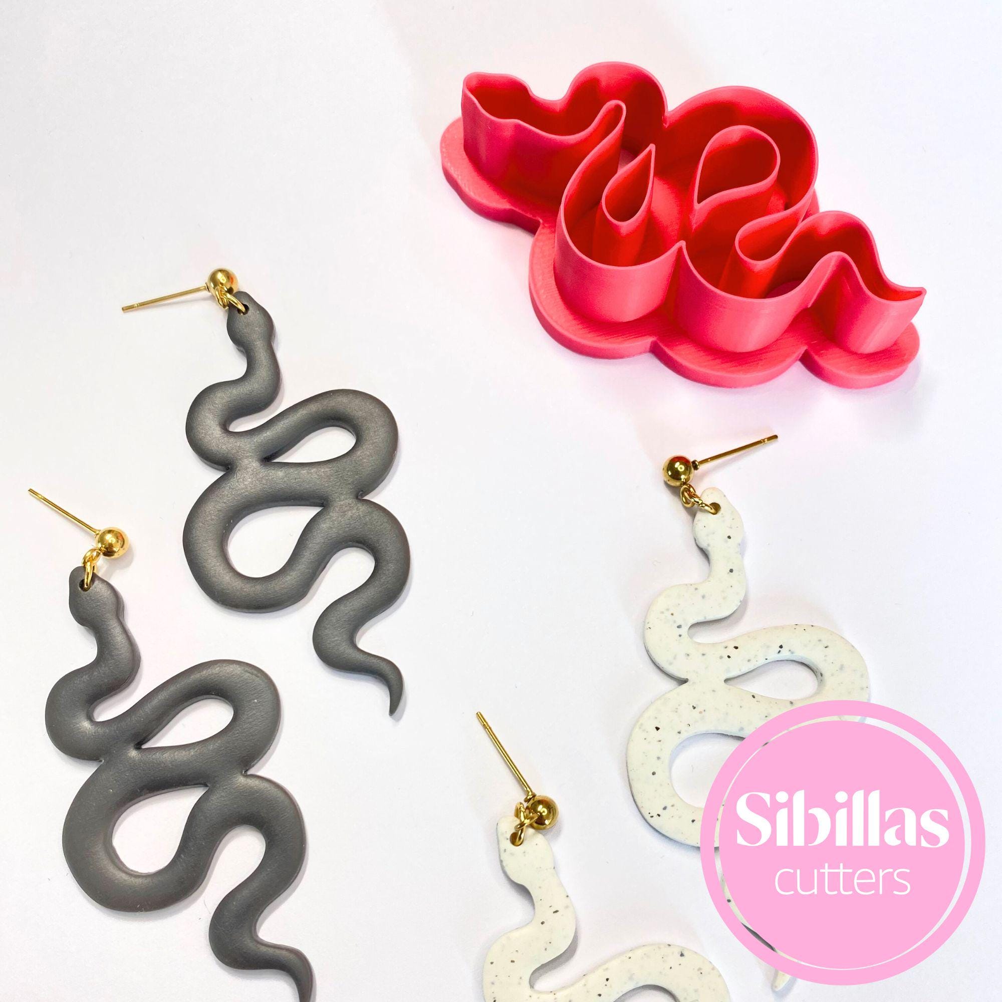 Snake-shaped earrings in gray and white with a pink mold and 'Sibillas cutters' branding.
