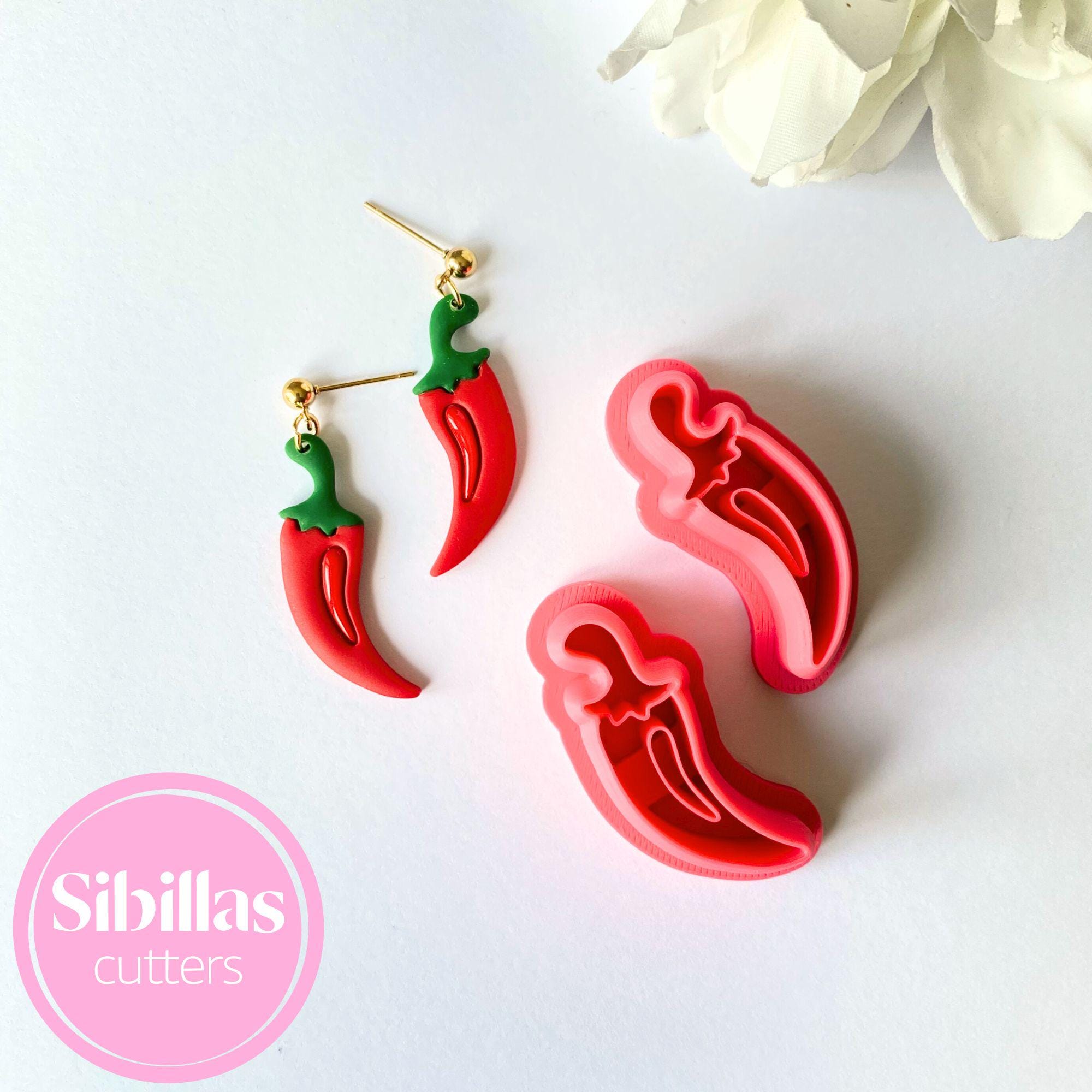 Red chili pepper-shaped earrings on a white background with 'Sibillas cutters' logo.