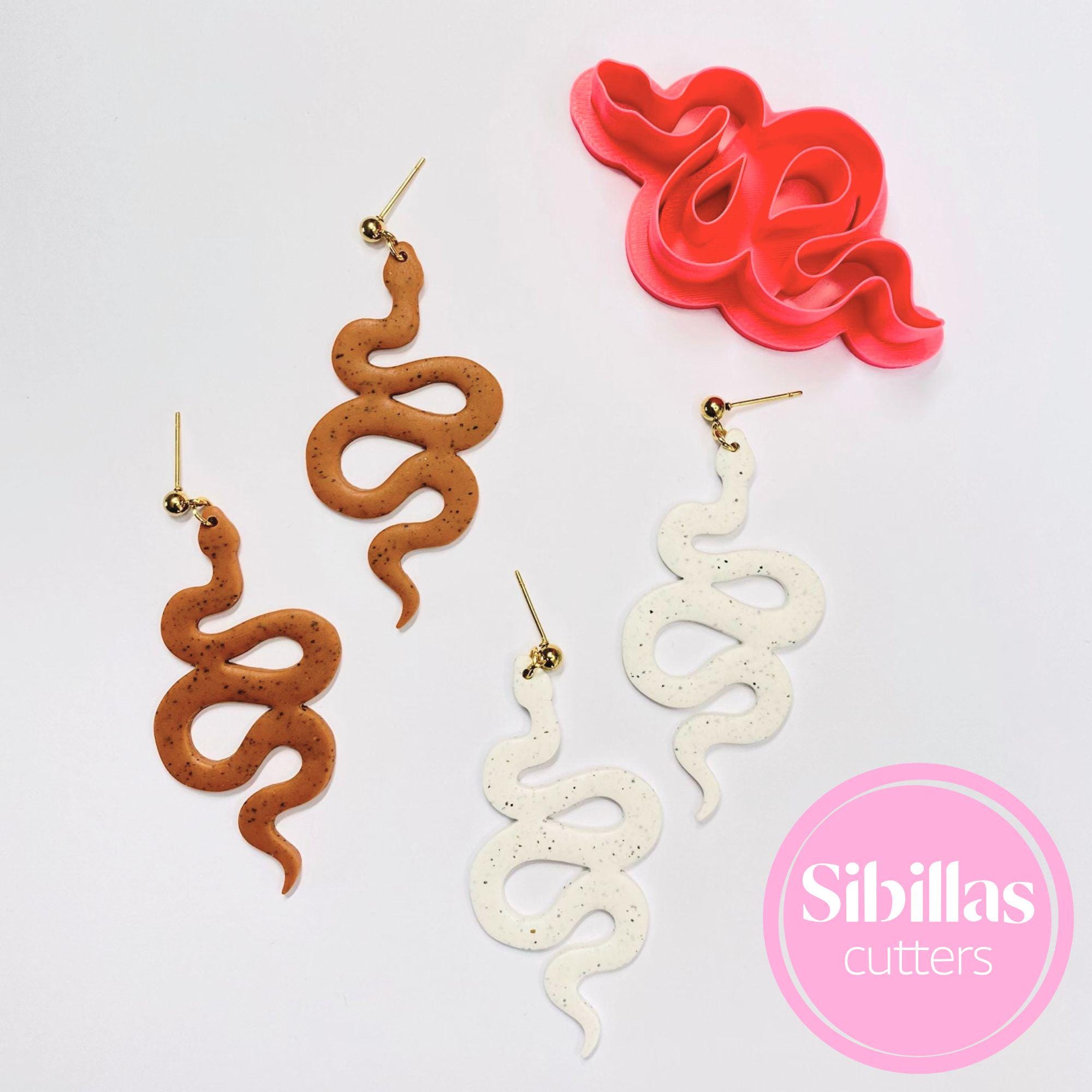 Snake-shaped earrings in brown and white with a pink tool and 'Sibillas cutters' logo on a light gray background.