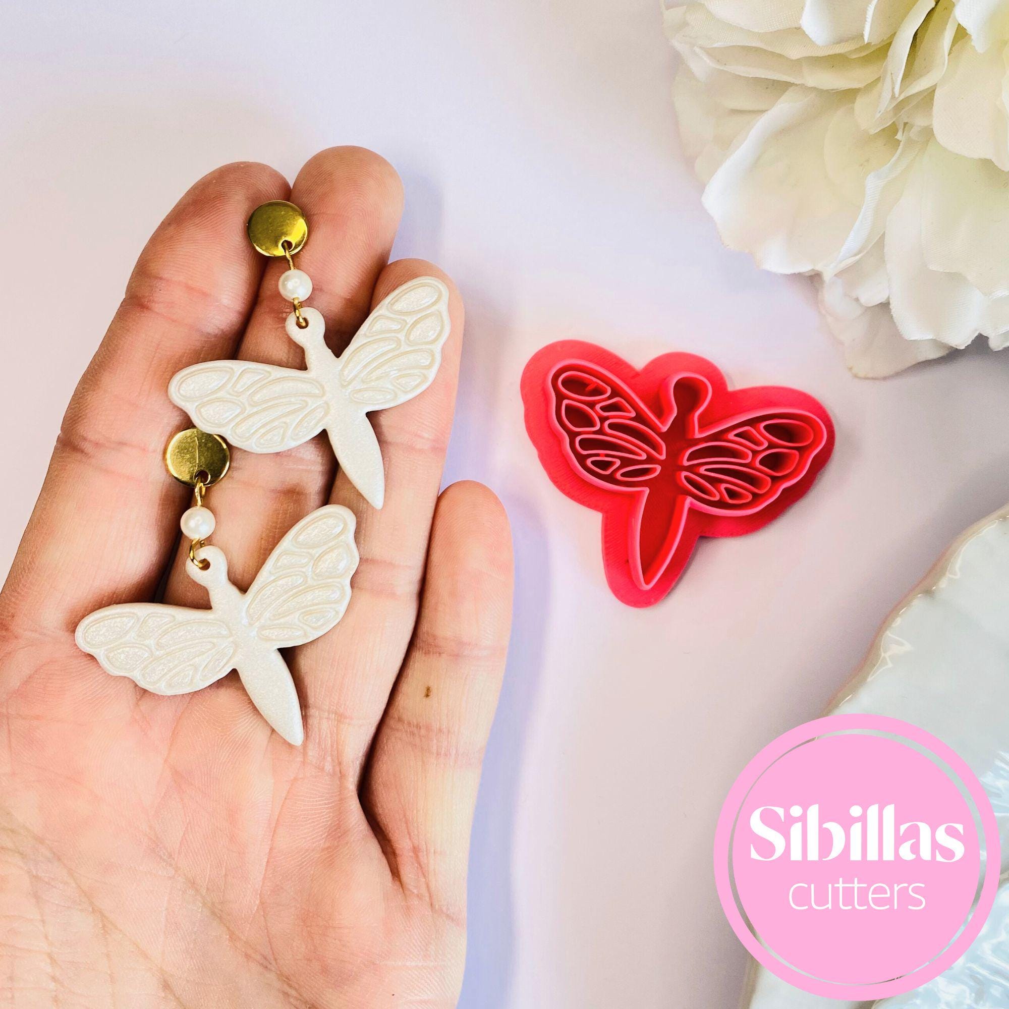 Butterfly-shaped cookie cutters held in a hand with a pink 'Sibillas Cutters' logo.