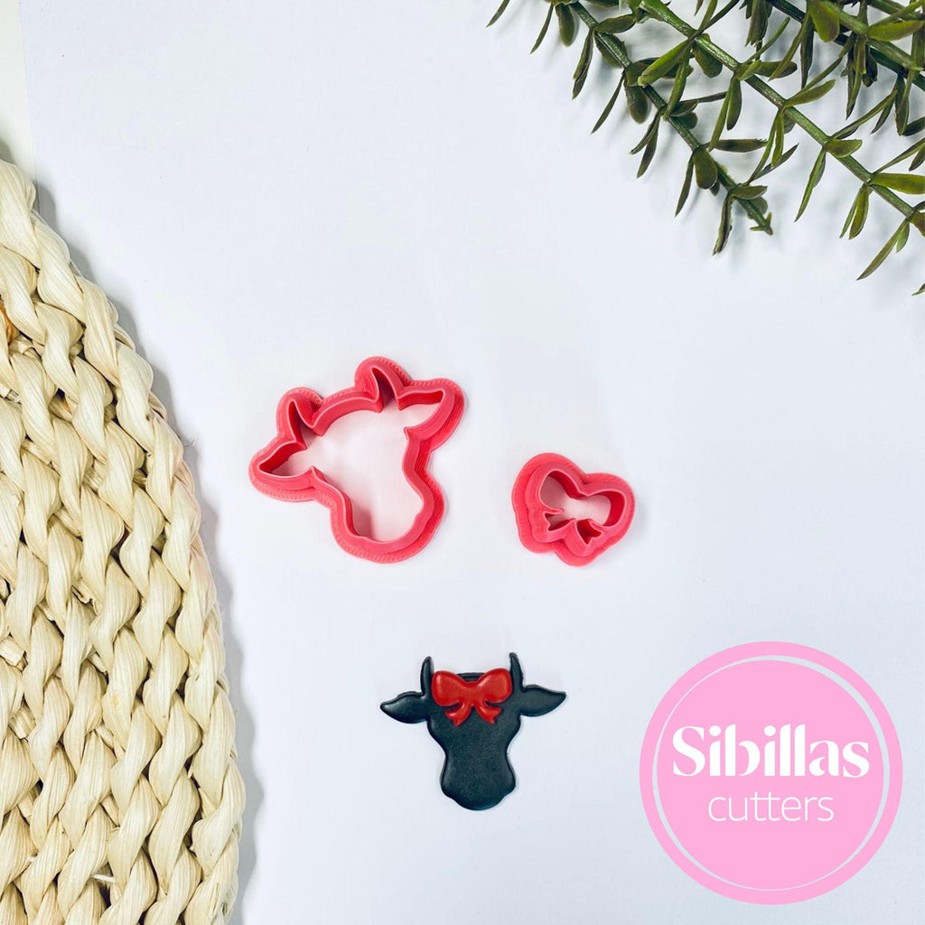 Red cookie cutters shaped like a cow and a heart on a white surface with a pink 'Sibillas cutters' logo.